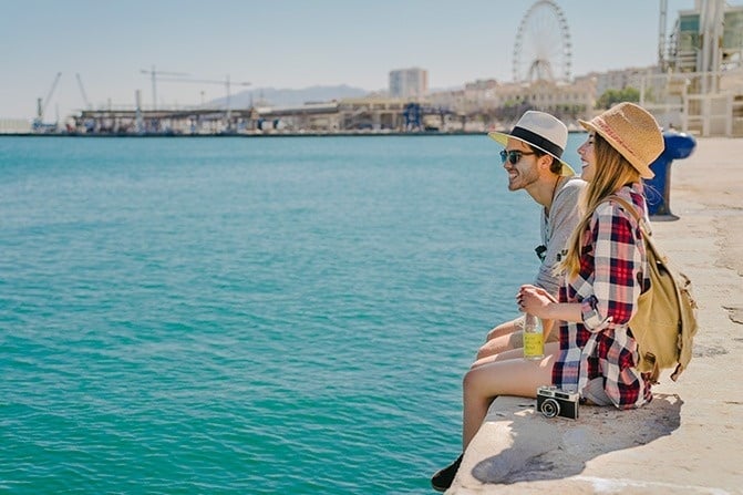 a man and a woman sit on a ledge overlooking the ocean