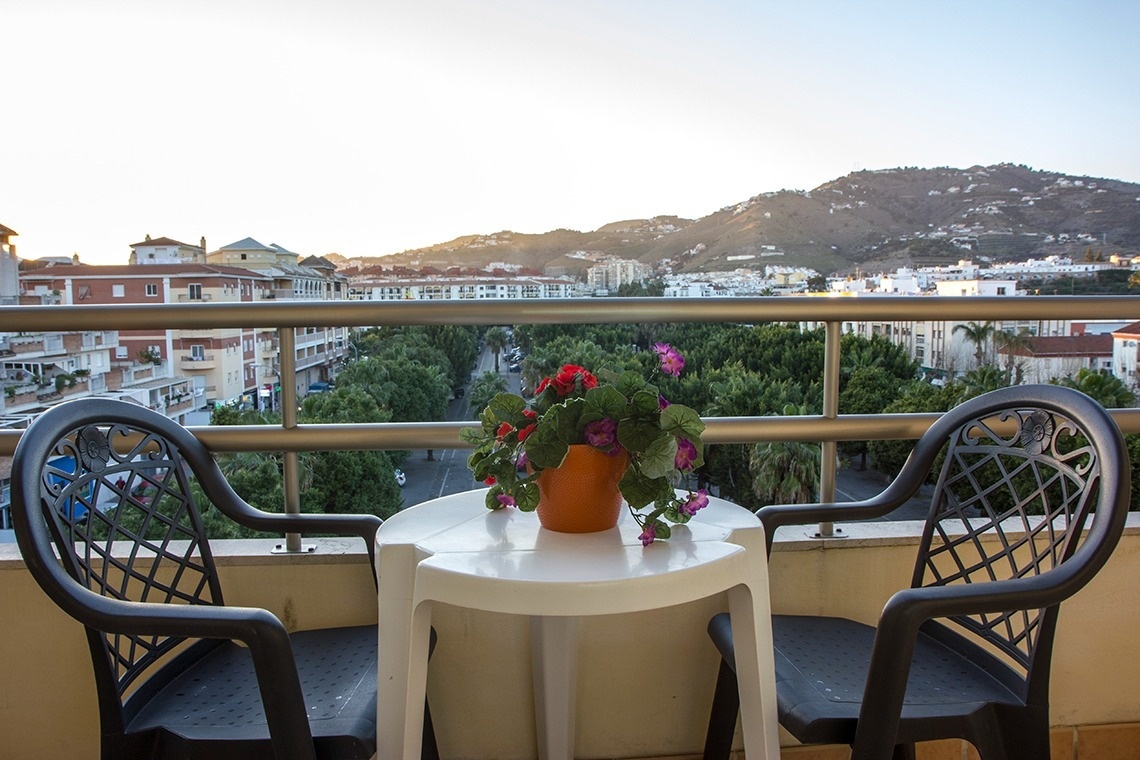 un balcón con dos sillas y una mesa con una maceta de flores encima