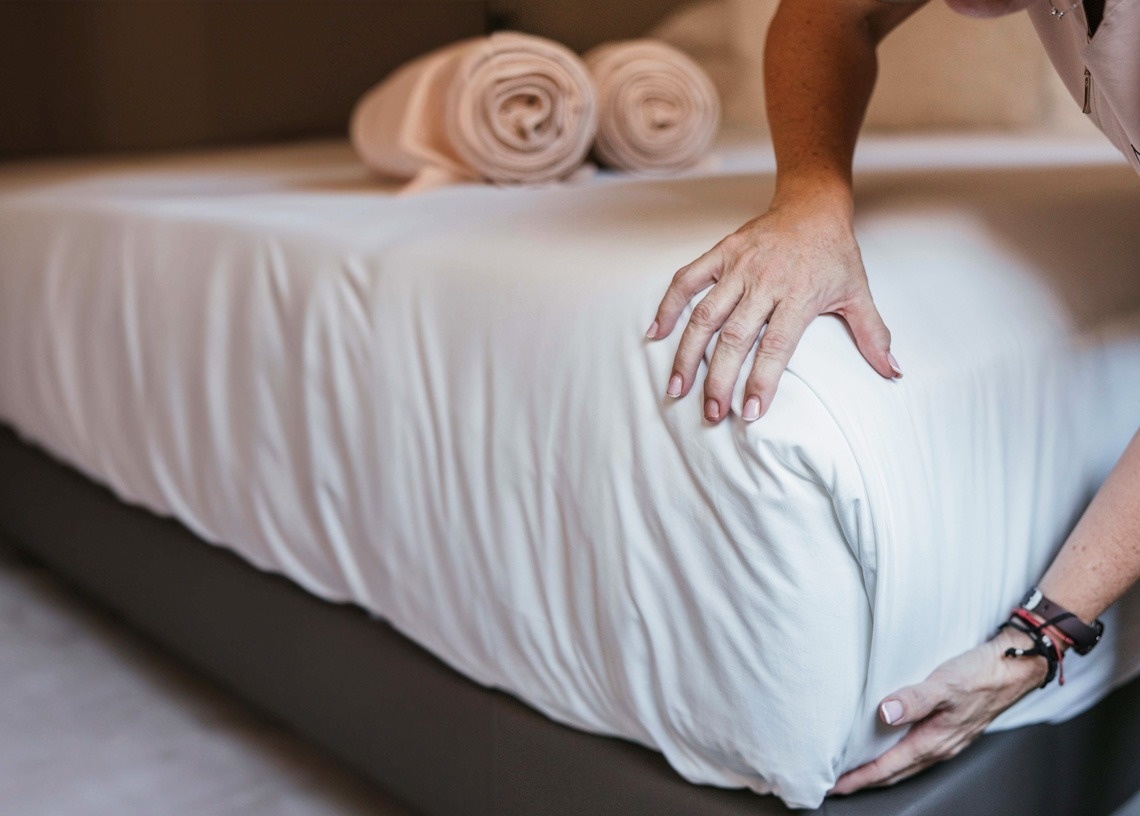 a woman is making a bed with white sheets