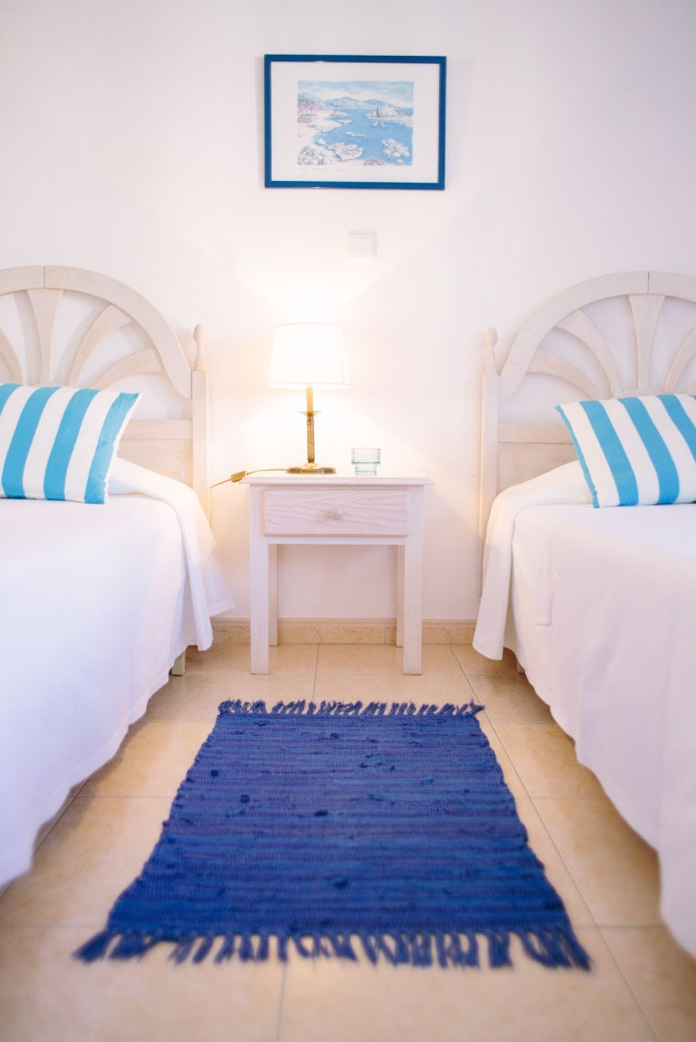 Habitación doble con camas individuales, ropa de cama azul y blanca, y alfombra azul. Apartamentos Dunas do Alvor, Torralvor | Web Oficial.