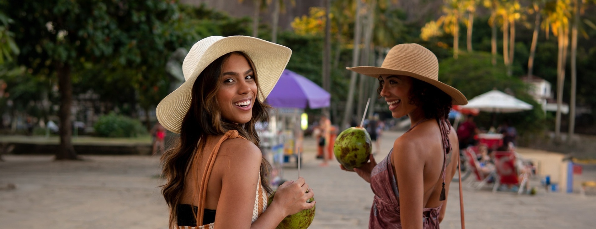 dos mujeres sonríen mientras sostienen cocos en la playa