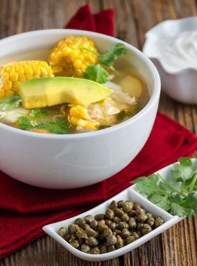 un tazón de sopa de pollo con maíz y aguacate en una mesa de madera .