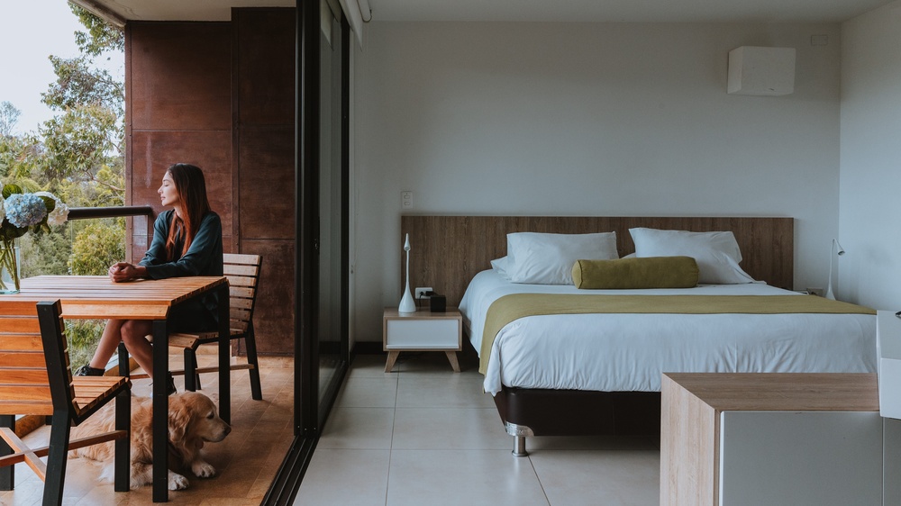 a woman sits at a table with a dog in front of a bed