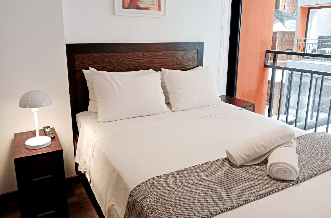Cozy hotel room with a queen bed, white linens, and a desk lamp, perfect for business travelers.