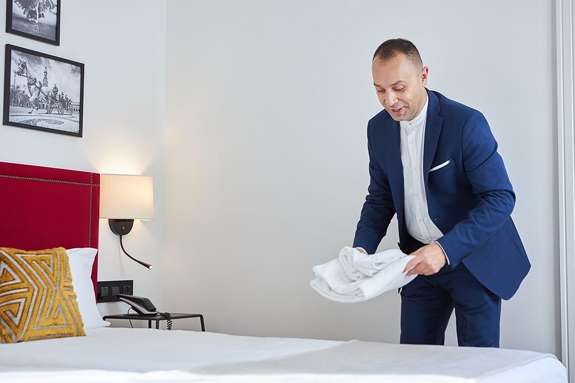 un hombre con traje azul sostiene una toalla blanca sobre una cama