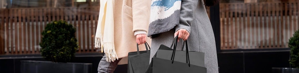 dos mujeres sostienen bolsas de compras mientras caminan por la calle .