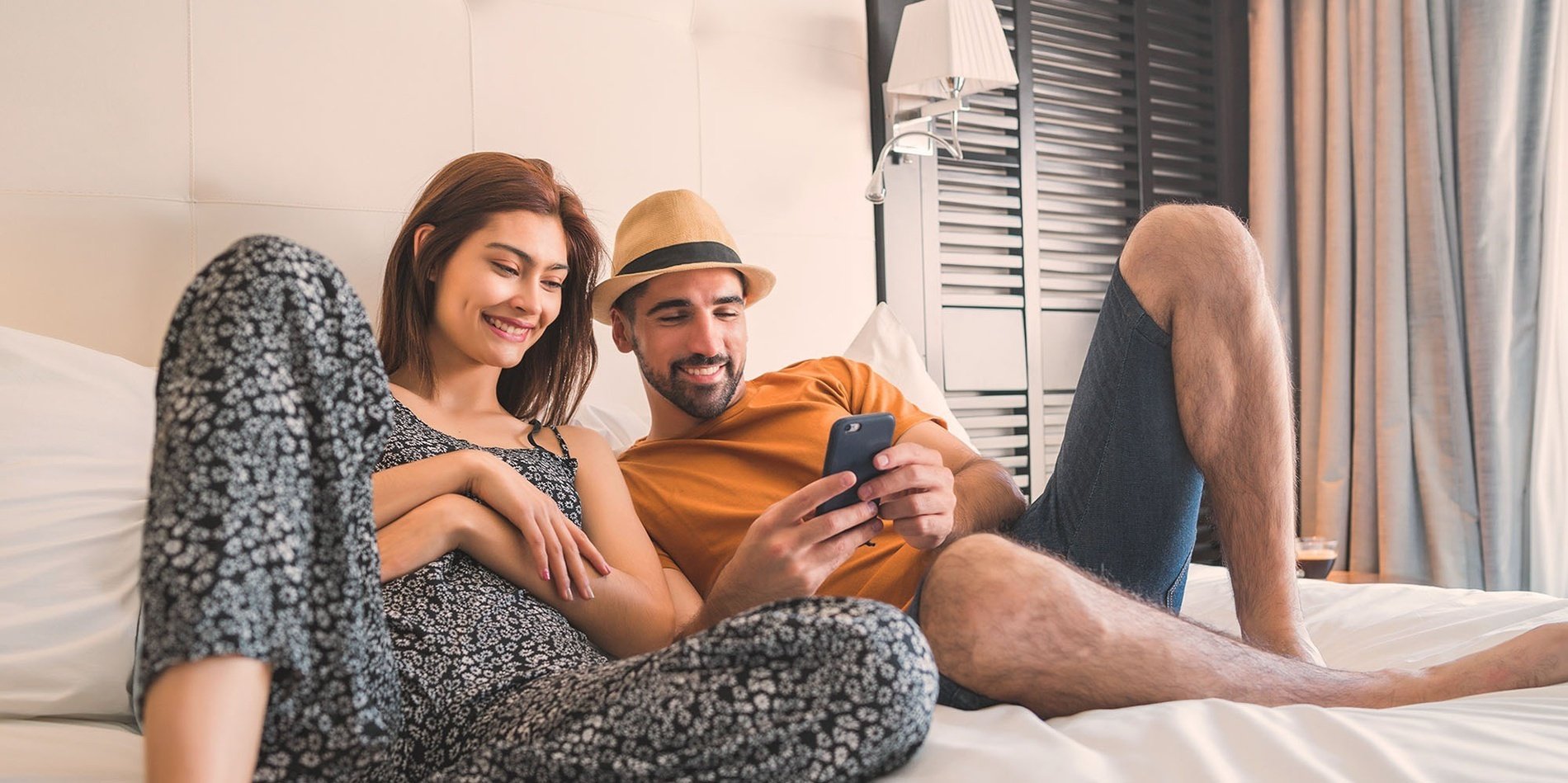 a man and woman sit on a bed looking at a cell phone