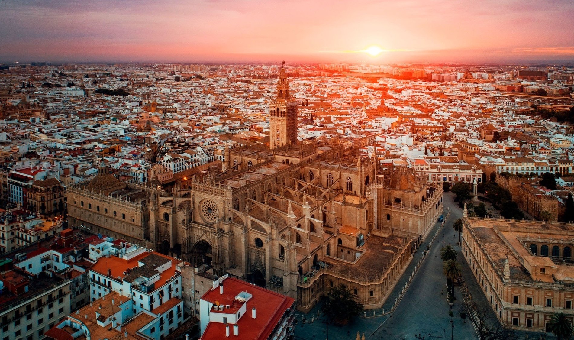 the sun is setting over a city with a large building in the foreground