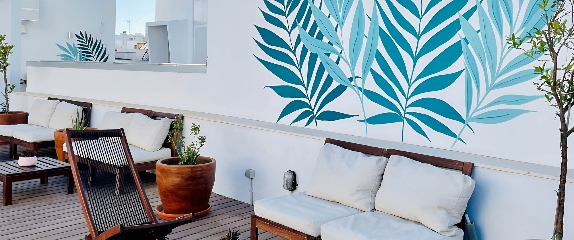 Terraza con sofás, plantas y mural tropical. U-Sense