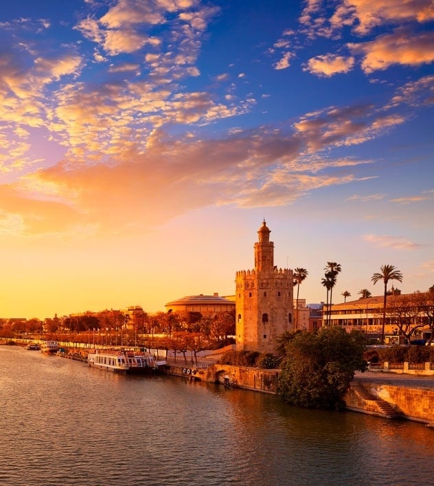 una torre de oro se encuentra al lado de un río al atardecer