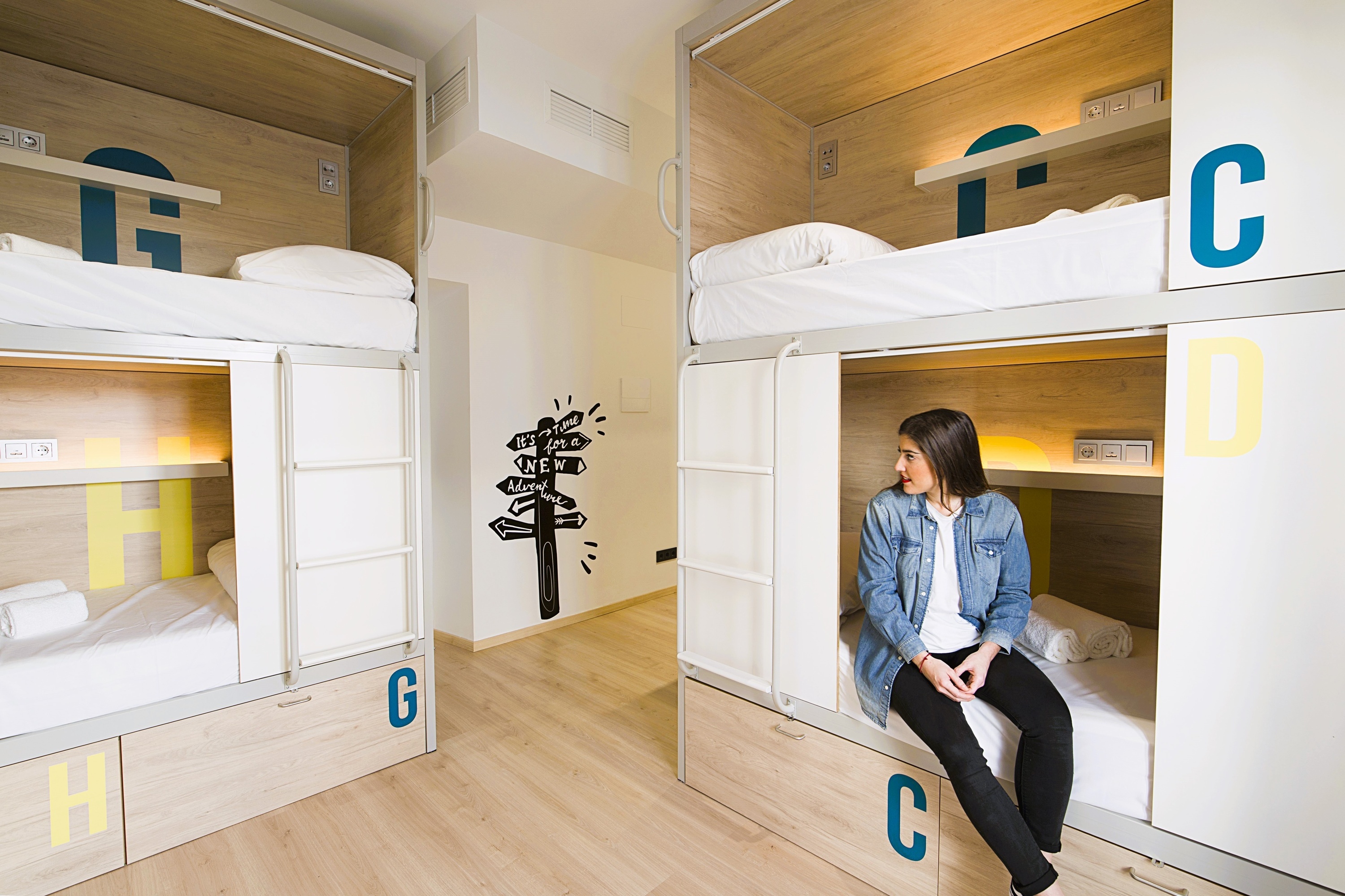 a woman sits on a bunk bed in a dorm room