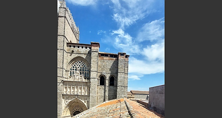 Vista de la Catedral de Ávila junto al Palacio Valderrabanos, con cielo azul y nubes.