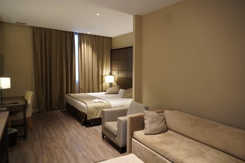 Una habitación de hotel moderna y acogedora con tonos neutros, que incluye una cama, un escritorio, un sofá y un sillón.