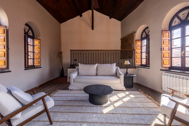 Salón con sofá y sillones, ventanas abuhardilladas y alfombra a rayas. Hotel Palacio Valderrabanos.