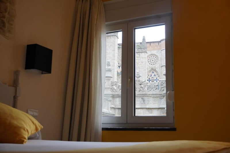 Una ventana en una habitación de tonos amarillos y beige ofrece una vista cercana de una catedral de piedra con detalles arquitectónicos intrincados.