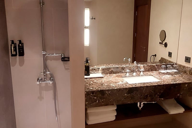 Se muestra un baño moderno con una ducha y un área de lavabo con encimera de mármol y espejo.