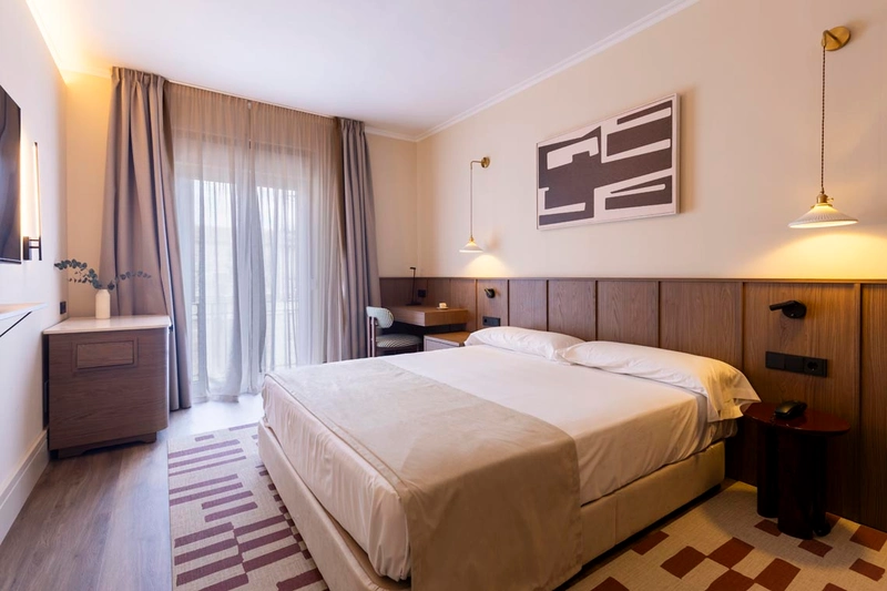Habitación de hotel cómoda con cama king, escritorio, cortinas y alfombra geométrica. Hotel Palacio Valderrabanos