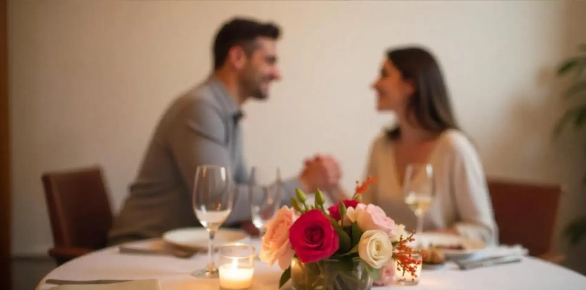 un hombre y una mujer están sentados en una mesa con copas de vino y flores .