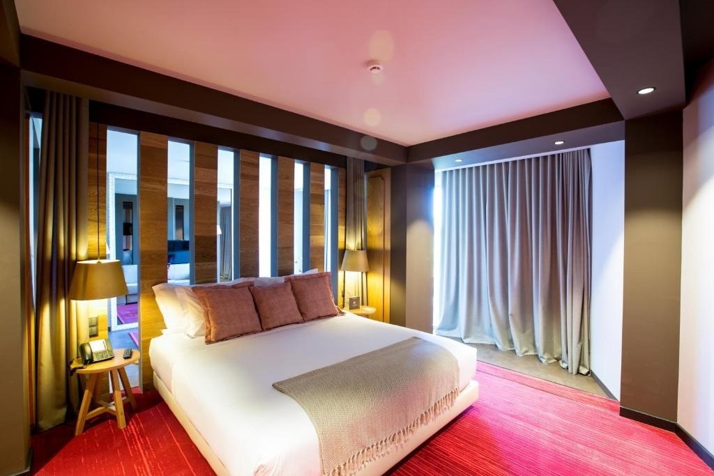 Una moderna habitación con una cama grande, alfombra roja, un panel divisorio de lamas de madera e iluminación cálida.