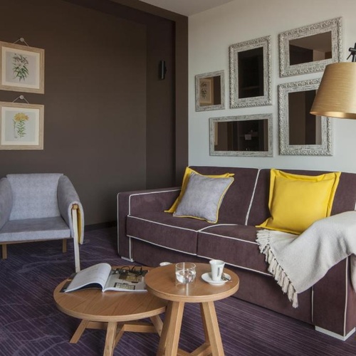 Lounge sofisticado em Vale d Azenha com sofá roxo, poltrona cinza e toques de amarelo.