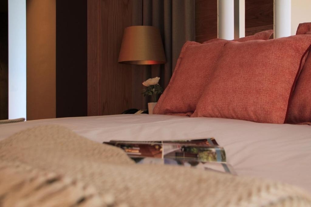 Un acogedor rincón de dormitorio presenta una cama con almohadas coral, una lámpara de noche encendida y una revista en primer plano.