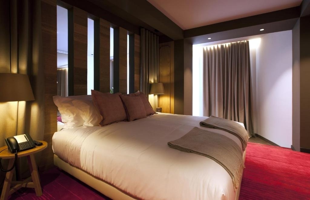 Una moderna habitación de hotel con una cama grande, alfombra roja, detalles de madera oscura y una iluminación cálida.