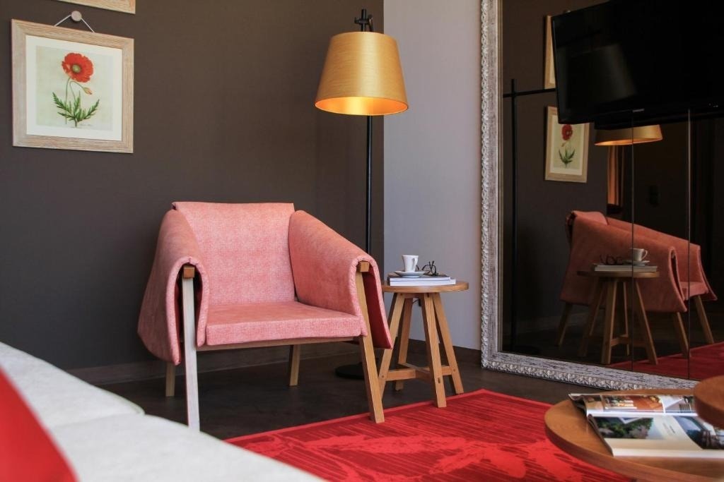 Una acogedora sala de estar presenta una butaca rosa, una alfombra roja vibrante, una mesa auxiliar de madera y un gran espejo de cuerpo entero.