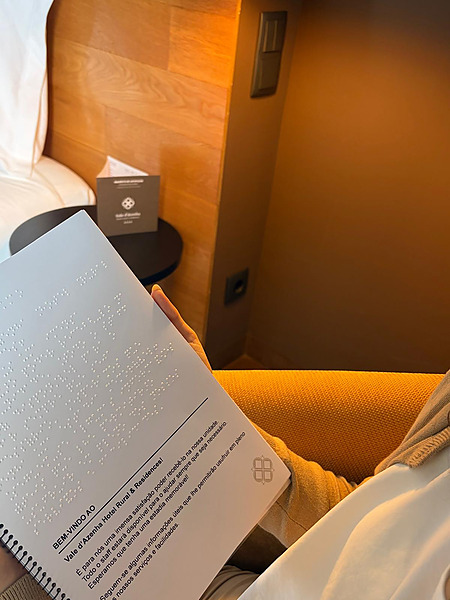 Huésped hojeando la guía en Braille sentado en la habitación, junto a la cama.