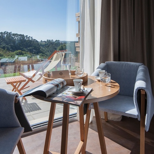 Mesa de centro com revista e cadeiras no Vale d'Azenha, com vista para o exterior.