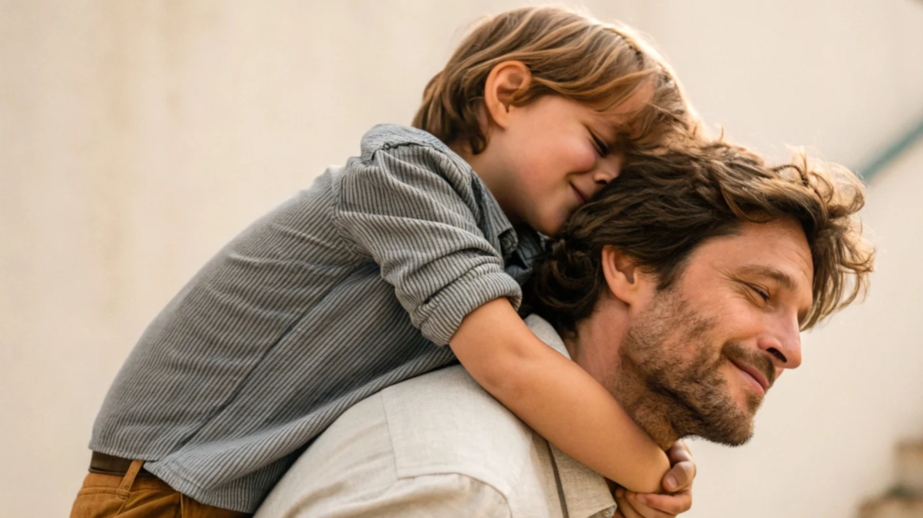Um homem sorri com os olhos fechados enquanto uma criança o abraça e apoia a cabeça em suas costas, também sorrindo com os olhos fechados, num momento de carinho e felicidade.