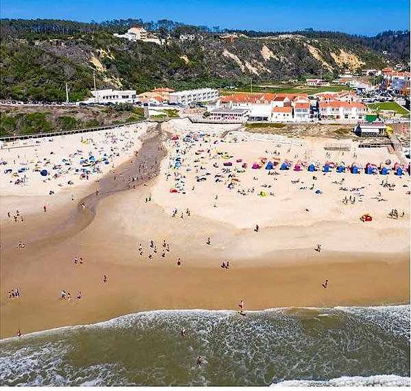 Vista aérea de la playa de Paredes da Vitória, con bañistas en la arena y el pueblo al fondo.