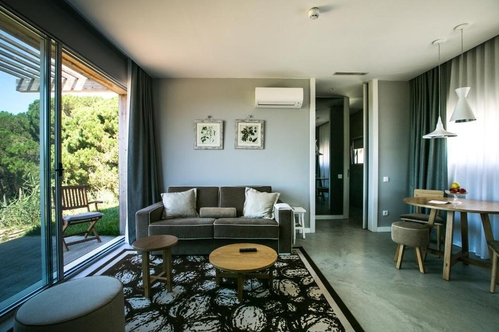 Una luminosa y moderna sala de estar y comedor, decorada con un sofá, una alfombra llamativa y arte botánico, se abre a un frondoso jardín a través de una gran puerta corredera de cristal.