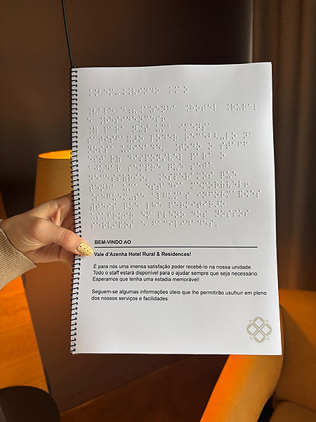 Guía de bienvenida de Vale d'Azenha impresa en Braille y en tinta, sostenida por una persona.
