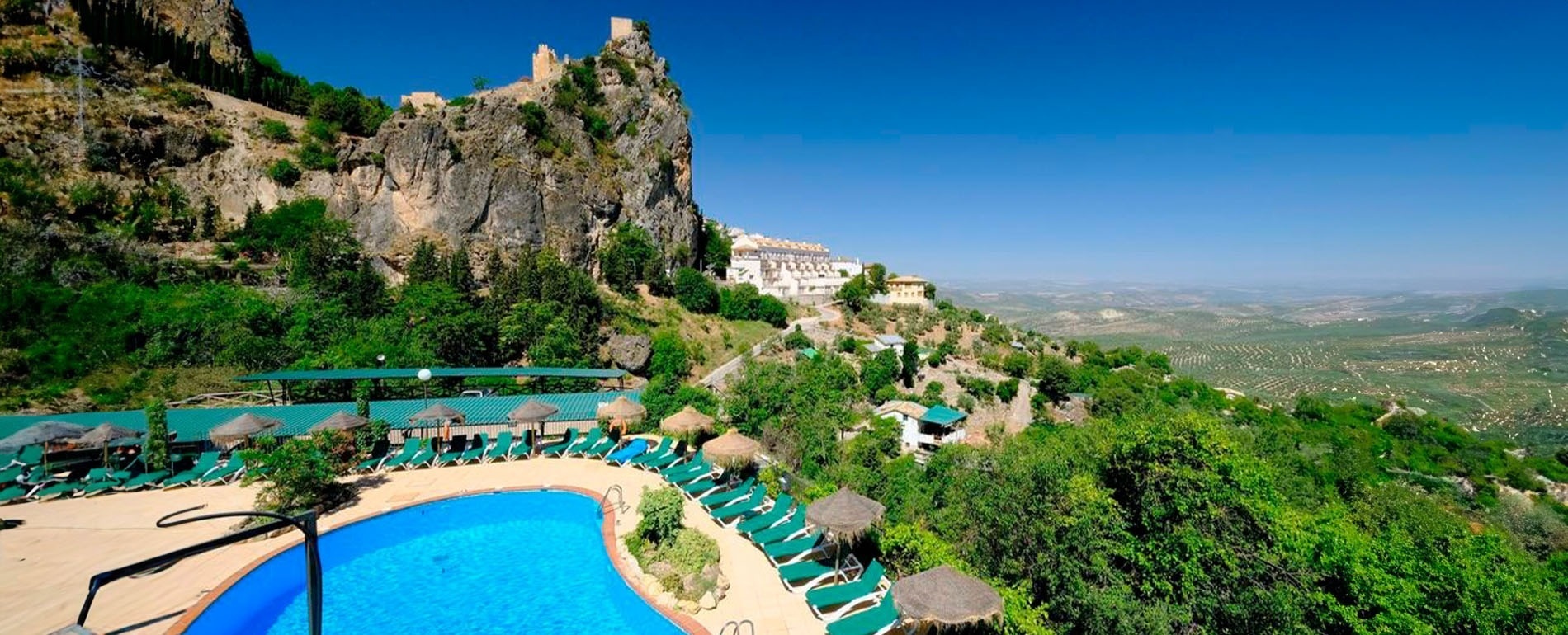 a large swimming pool surrounded by chairs and umbrellas with a castle in the background