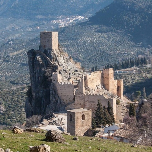 un castillo en la cima de una montaña con un pueblo al fondo