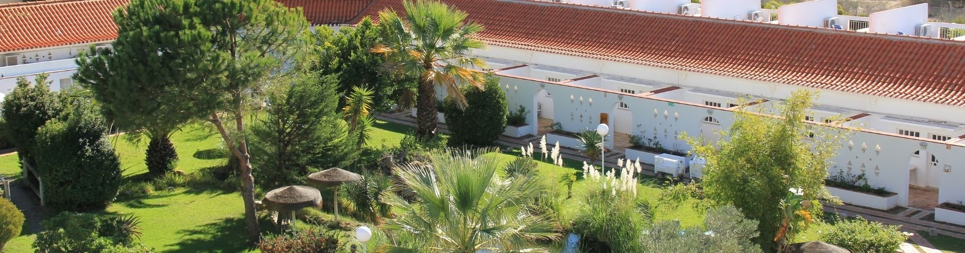 a white building with a red tile roof is surrounded by a lush green garden