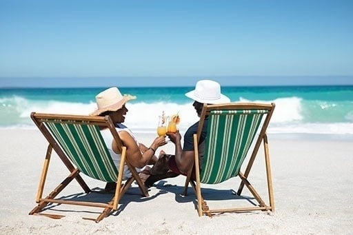 a man and a woman are sitting in lawn chairs on the beach drinking cocktails