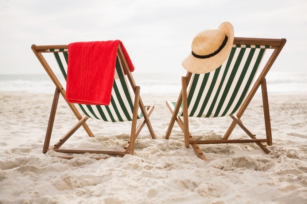 two lawn chairs on the beach with a red towel and a hat