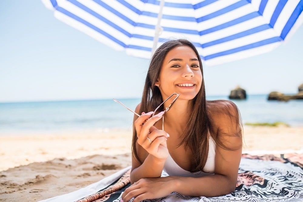 una mujer acostada en la playa con un paraguas y gafas de sol