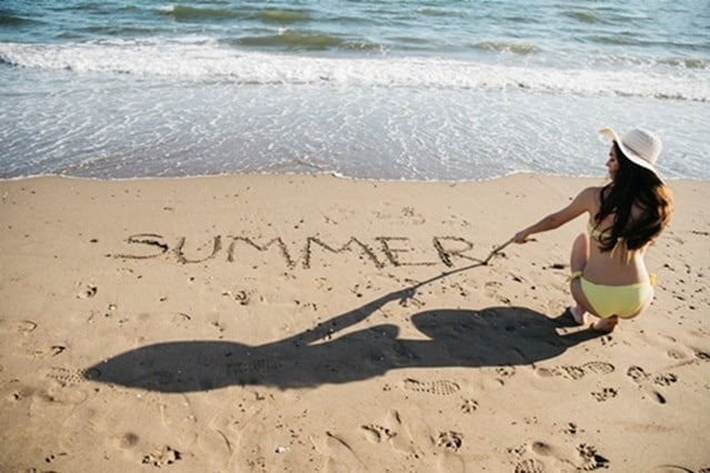 una mujer escribe la palabra verano en la arena