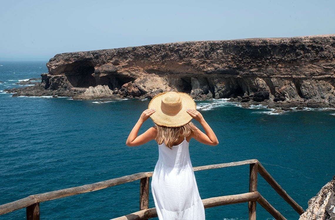 a woman in a white dress and straw hat looks out over the ocean