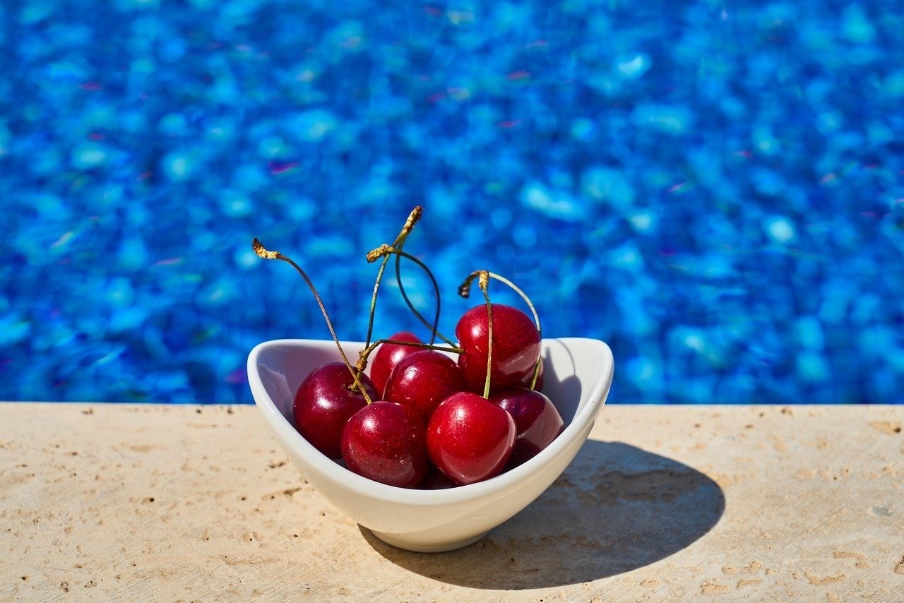 a bowl of cherries sits in front of a swimming pool