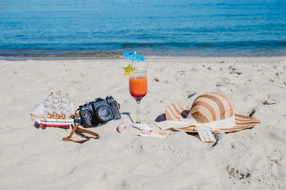 a beach scene with a camera a hat and a drink