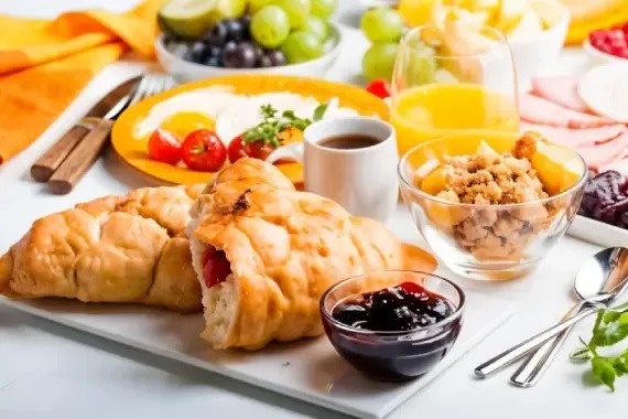 a table topped with a variety of food including croissants , eggs , fruit , cereal and coffee .