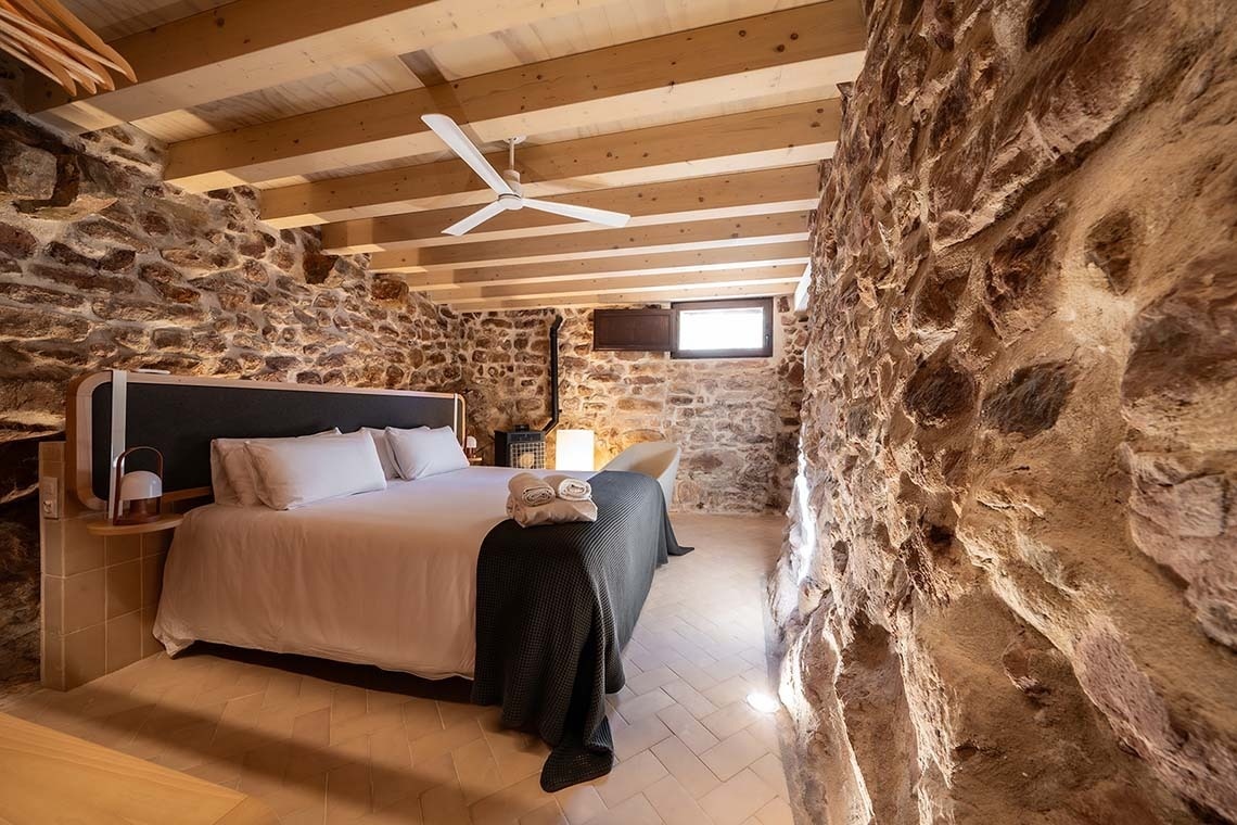 Acogedora habitación en Apartamentos Vilafames Antic Palau con paredes de piedra y techo de madera.