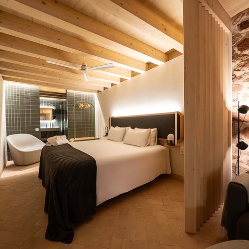 Modern bedroom in Apartamentos Vilafames Antic Palau, featuring stone walls and wood beams.
