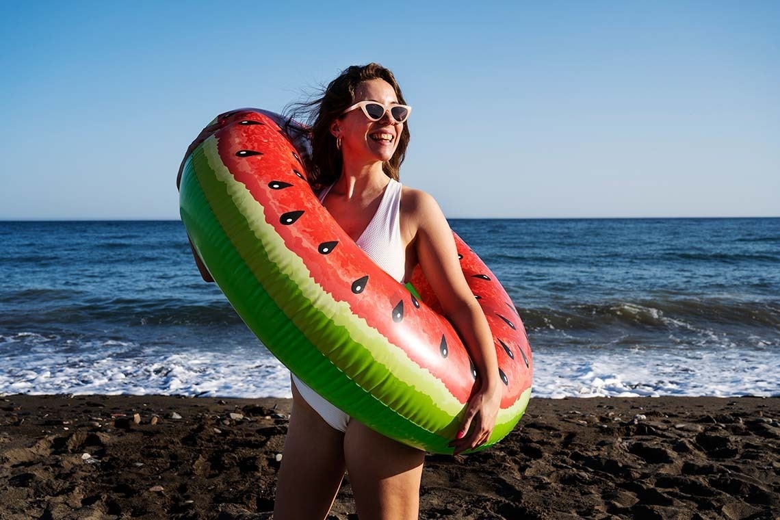 una mujer sostiene un círculo inflable en forma de sandía en la playa