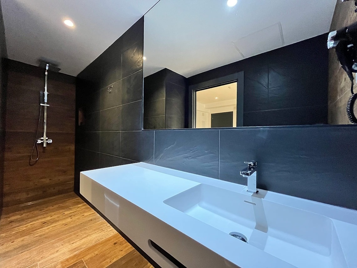 un baño con azulejos negros y un lavabo blanco