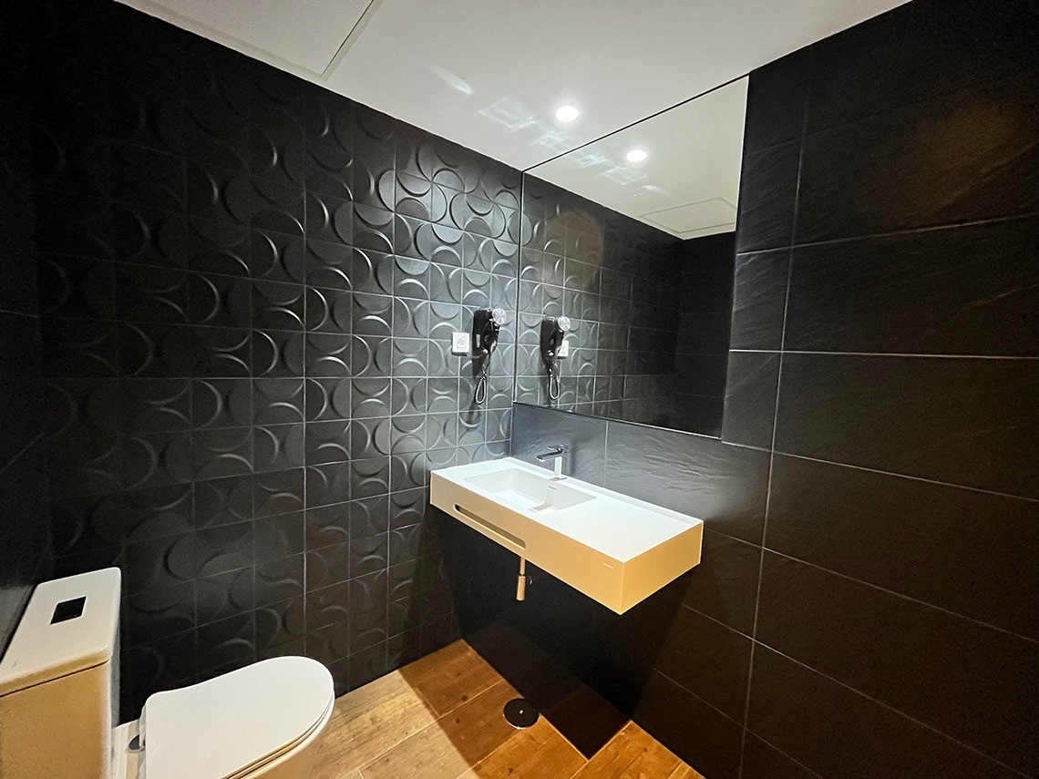 un baño con azulejos negros y un lavabo blanco