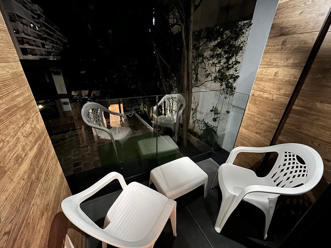 dos sillas blancas y un taburete en un balcón por la noche